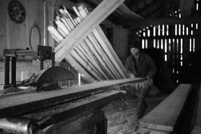 A worker saws lumber by hand in a sawmill